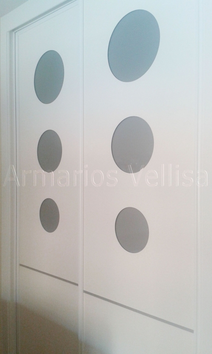 Armario en habitación juvenil. Puertas correderas: 2 Modelo: Círculos con cristal color aluminio mate. Y una línea de aluminio horizontal por debajo círculos. Panel: Blanco veta poro, melamina. Color base: Blanco melamina