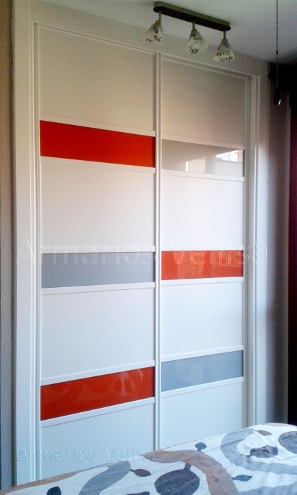 Armario empotrado en dormitorio principal. Puertas correderas: 2 Modelo franjas horizontales. Combinado con cristal naranja y gris plata. Resto, tablero blanco, melamina