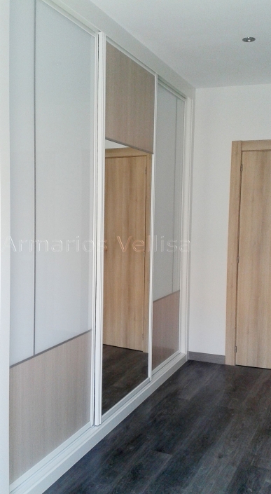 Armario a medida en dormitorio. Puertas correderas: 3 Puerta central espejo y tablero color arena separado por junquillo aluminio mate a 200 cm. altura. Puertas laterales: Cristal blanco separado en vertical con junquillo aluminio mate y separado en horizontal tablero color arena. Color base: Blanco, melamina